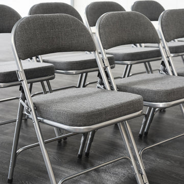 Rows of Comfort Deluxe Metal Folding Chairs with grey upholstery in a hall or meeting space
